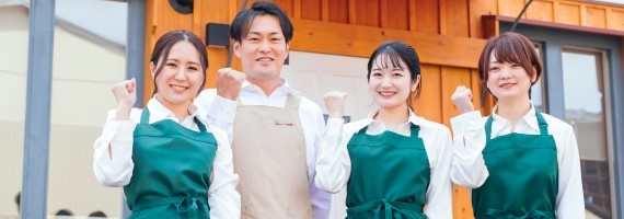 流通の作業風景として、建物の前にエプロンを着た4人が立っている画像です。